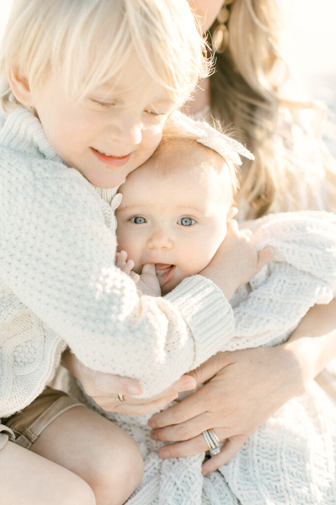 A heartwarming image capturing a mother holding two children, wrapped in spring sweaters, emanating cozy yet fresh vibes. The scene radiates warmth and familial closeness, epitomizing the comforting essence of springtime.