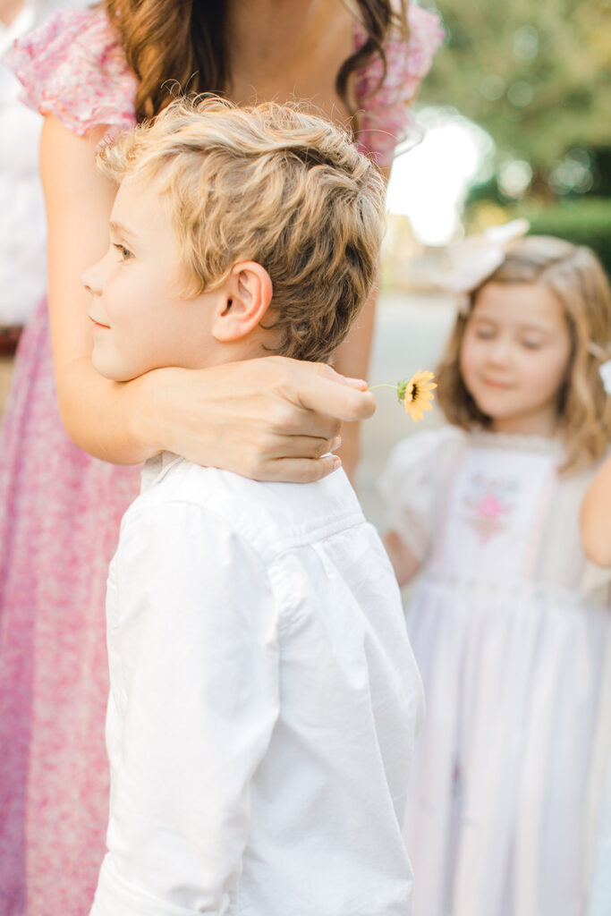 A heartwarming image capturing a little boy being affectionately loved by his mother, adorned in a stunning floral dress. The scene radiates love, warmth, and a charming embrace, epitomizing the joy of familial bonds in a beautifully captured moment.